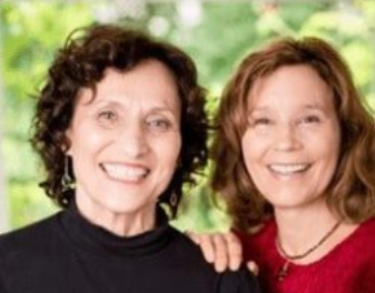 Two smiling women with curly hair, one in a black top and the other in a red top, stand close together, as if capturing joyous moments for their latest videos against a green, blurred background.